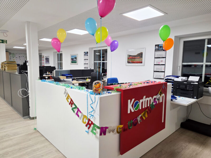 Geschmückter Empfangsbereich bei Korfmann mit bunten Luftballons, Girlanden und Glückwunschbanner.