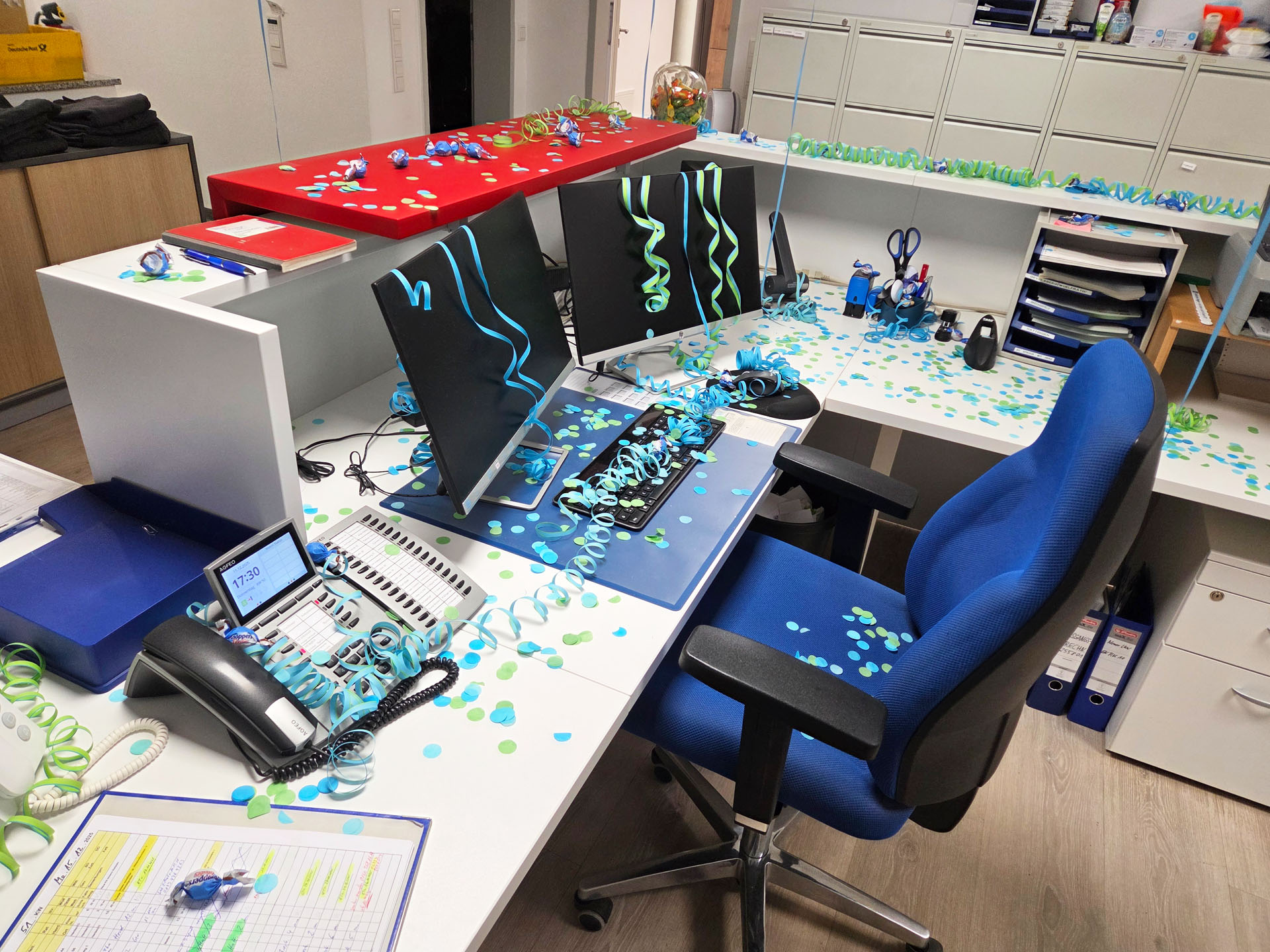 Arbeitsplatz im Büro mit Konfetti und Luftschlangen auf Schreibtisch und Monitoren – Dekoration zur Verabschiedung.